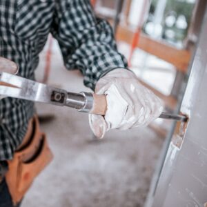 A mason uses a hammer and chisel on a building under construction with his hands on gloves